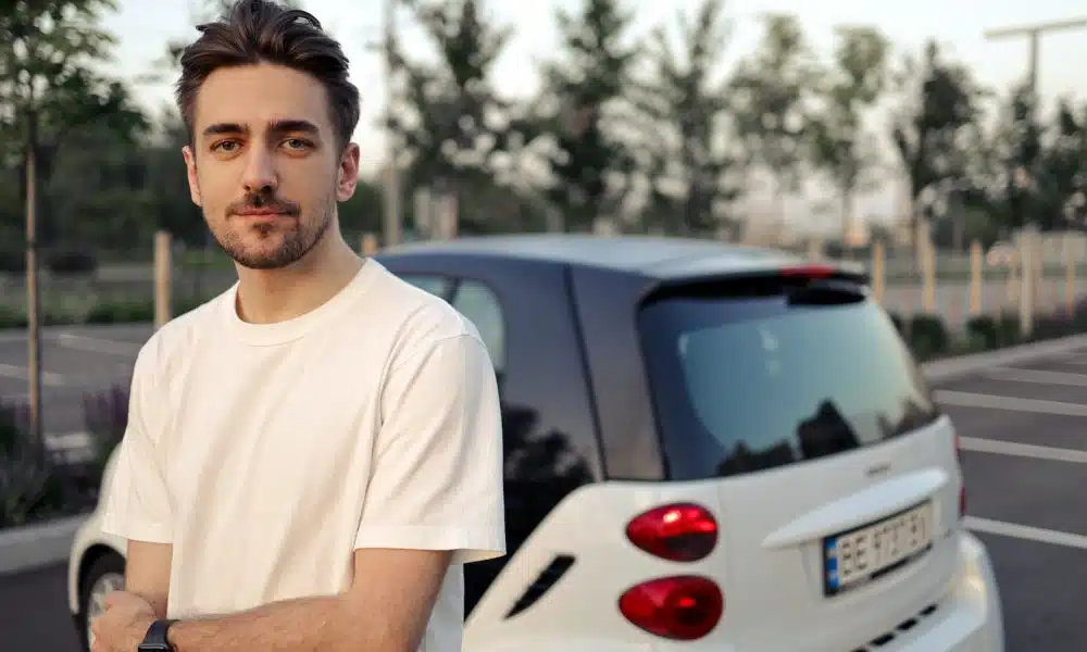 man in white crew neck t-shirt standing beside white car during daytime